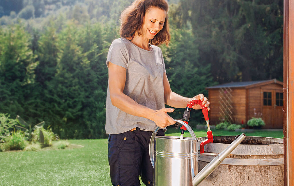 A woman filling rainwater from a rain barrel into a watering can.