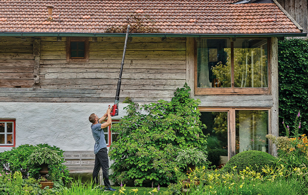 A man cleaning a rain gutter with a cordless leaf blower and a gutter kit.