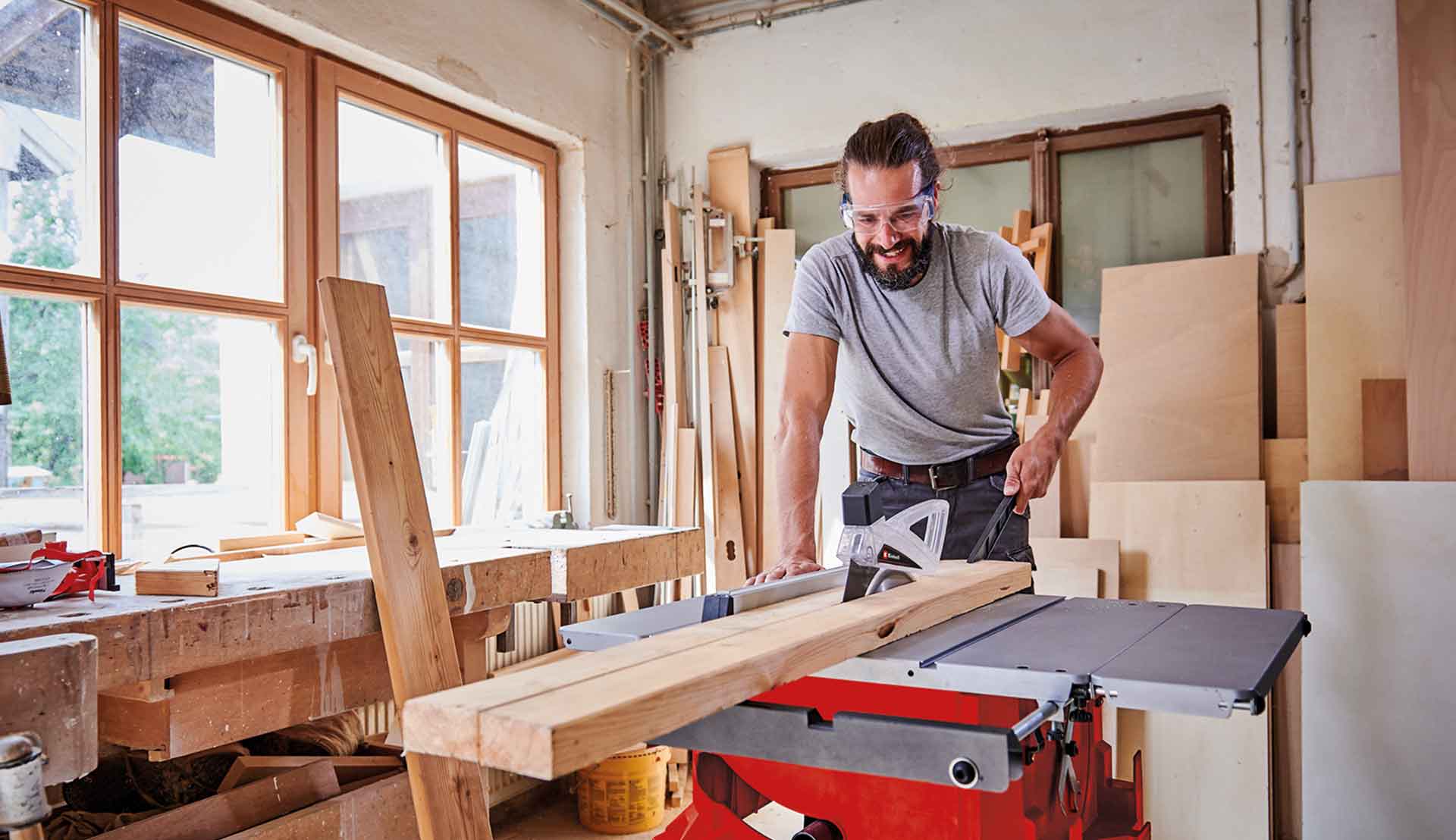 A man cutting a long wooden plank using a table saw.