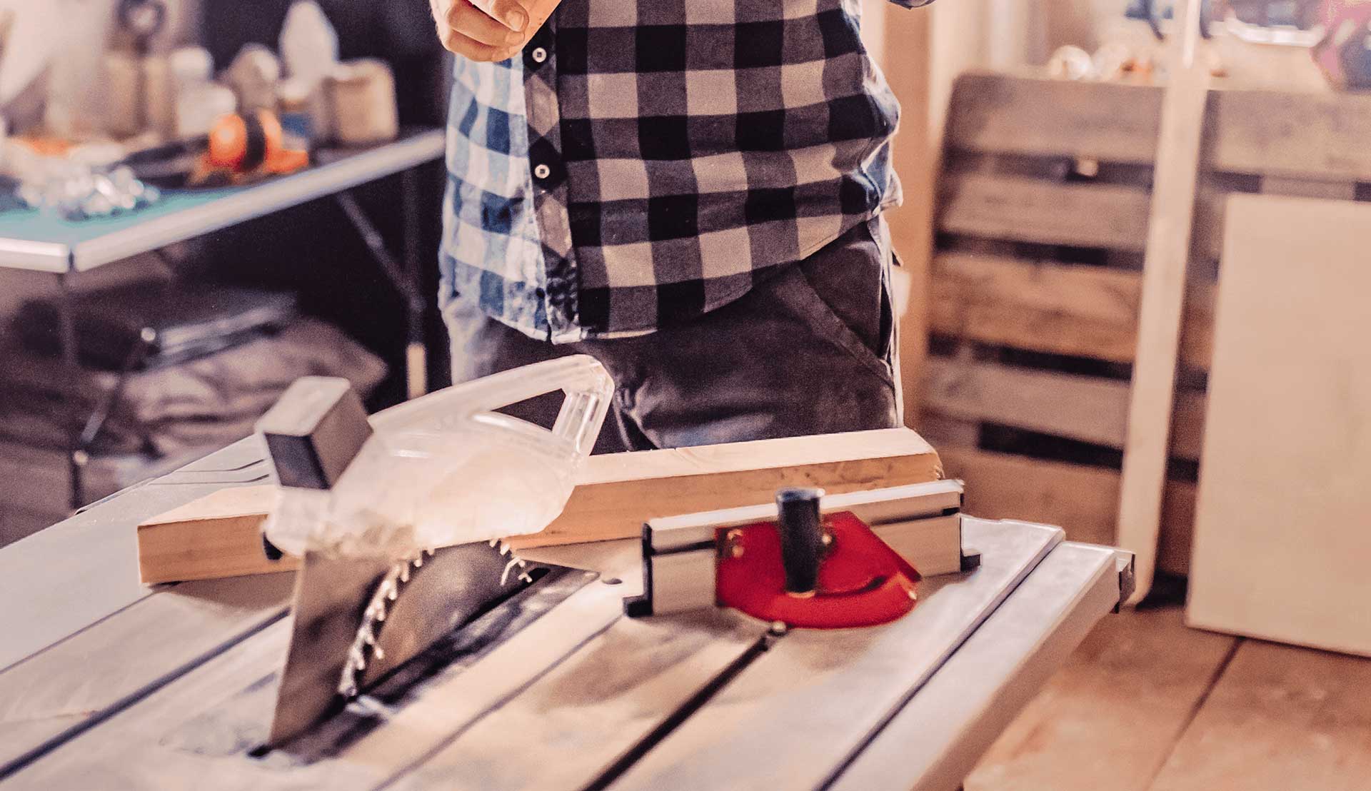 A man using an angle guide on a table saw to cut a wooden plank at the correct angle.