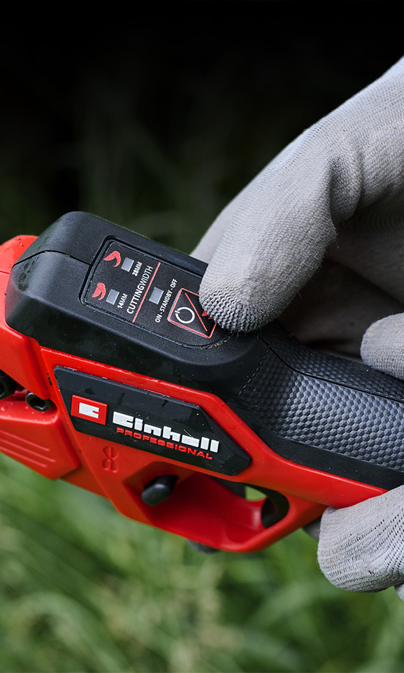 Close-up of a red Einhell cordless device with a gloved hand adjusting its mode.