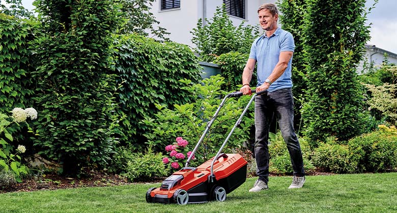 A man in his garden, mowing the lawn with a cordless lawnmower.